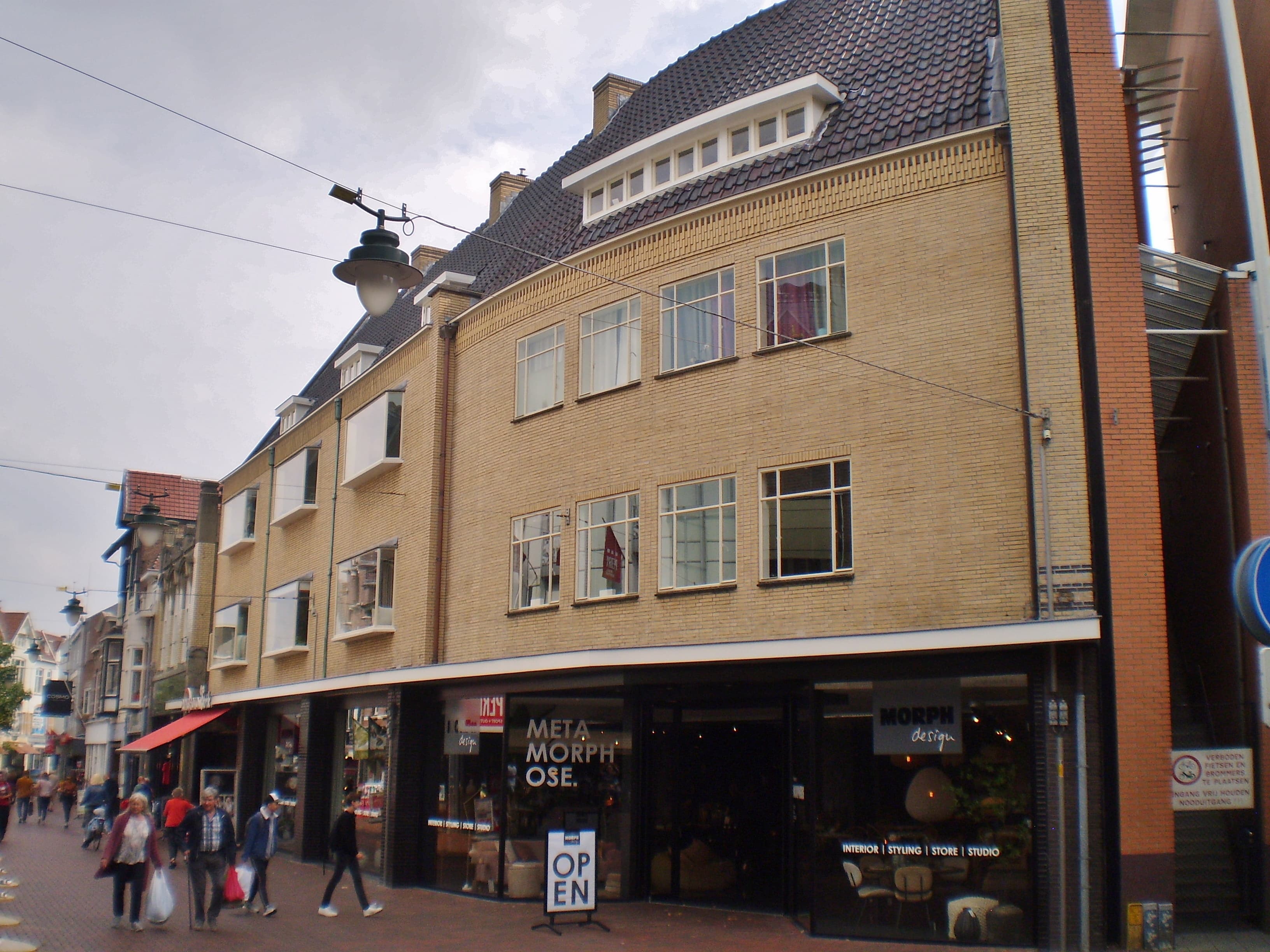 Voetgangers met boodschappentassen lopen door de bestrate Kerkstraat in Hilversum, langs winkelpanden, onder een bewolkte lucht